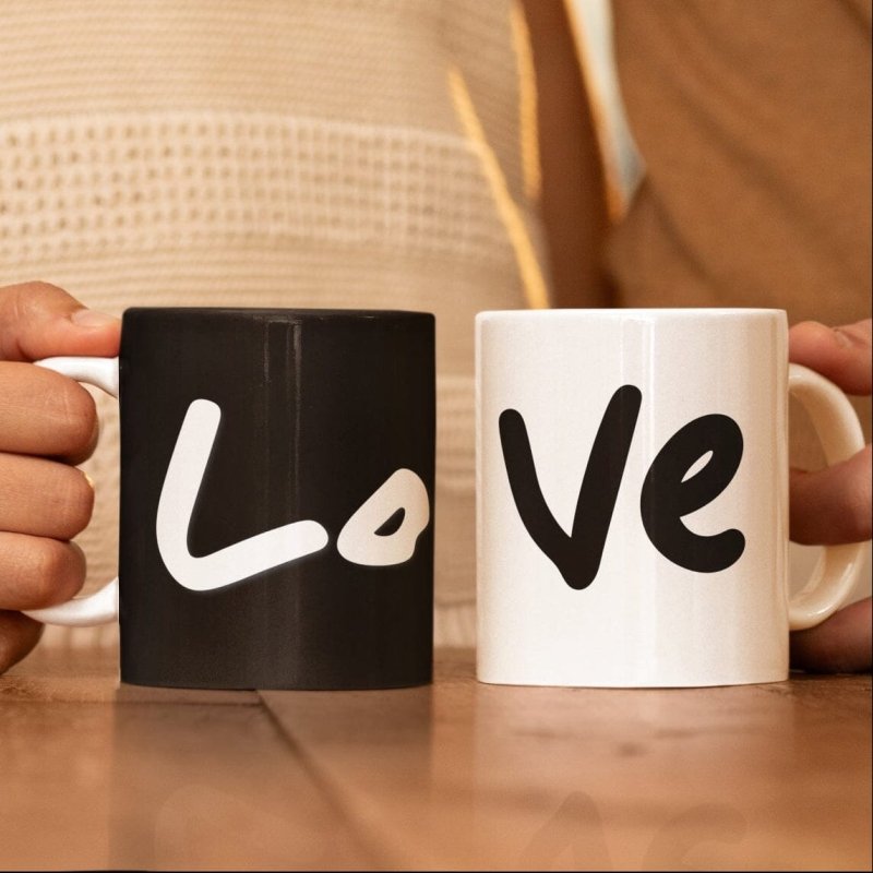 Two mugs, one black and one white, with 'Love' written on them, held by a person.